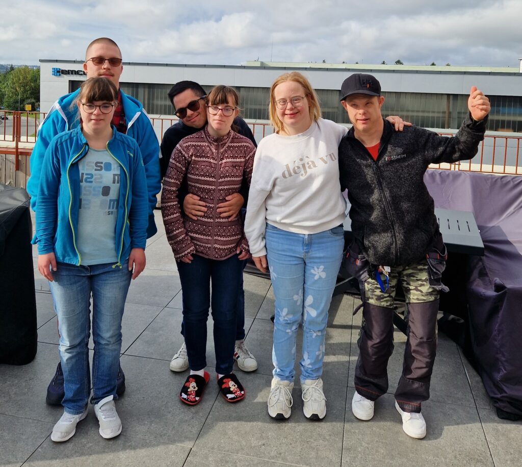 6 personer med Downs syndrom holder rundt hverandre og smiler til kamera